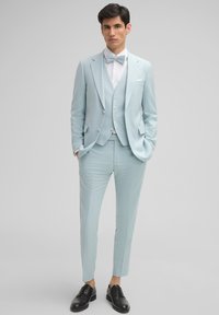 Hellblauer Anzug mit strukturiertem Blazer, Weste und Slim-Fit-Hosen. Der Stoff hat ein strukturiertes Muster und wird mit einem weißen Hemd und einer Fliege kombiniert.