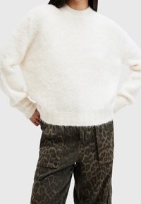 Weiße, flauschige Sweater mit rundem Ausschnitt und gerippten Bündchen, kombiniert mit olivfarbenen Cargo-Hosen mit einem braunen Leopardenmuster.