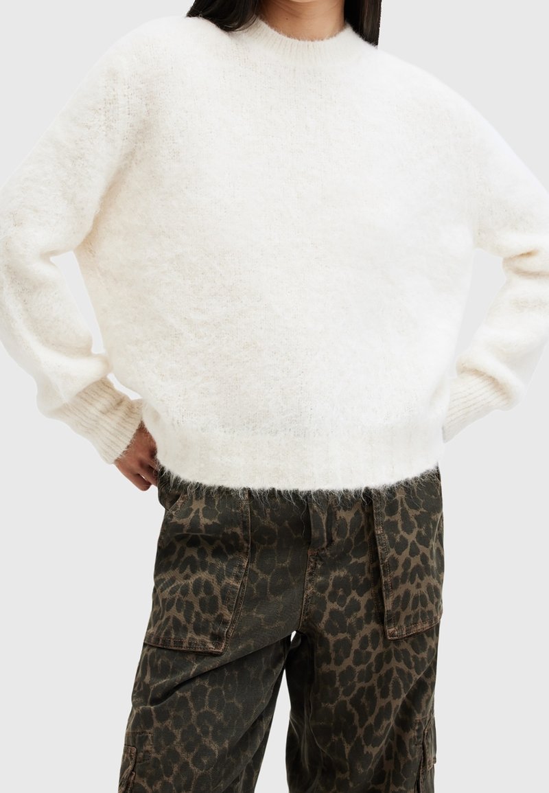 Weiße, flauschige Sweater mit rundem Ausschnitt und gerippten Bündchen, kombiniert mit olivfarbenen Cargo-Hosen mit einem braunen Leopardenmuster.