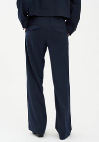 Marineblauwe pinstriped broek met een ontspannen pasvorm, voorzien van een trekkoord in de taille, twee achterzakken en een soepele, gestructureerde stof.