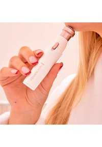 Remington gezichtsbeharingstrimmer, witte behuizing met roségouden accenten, slank ontwerp, vastgehouden in de hand nabij het gezicht, met licht gepolijste nagels.