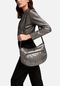 Borsa metallizzata grigia dalla forma a mezzaluna, con tasca frontale con cerniera e dettagli in metallo color oro. Texture liscia con motivi sottili.