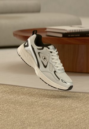 Weißer Sportschuh mit schwarzen Akzenten, Netzpaneelen, strukturierter Sohle und Logo; verfügt über ein Schnürdesign und einen hinteren Zuglasche für einfaches An- und Ausziehen.