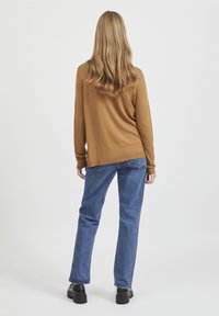 Bruine lange mouwen top met een losse pasvorm, gecombineerd met blauwe rechte jeans en zwarte plateau schoenen. Eenvoudige, effen kleuren; geen patronen.