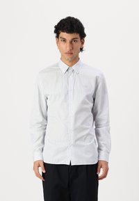 Camisa de manga larga a rayas blancas y azul claro con cuello abotonado. Presenta un logotipo en el pecho y una tela suave y ligera.