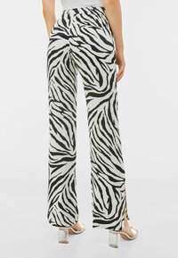 Květované široké kalhoty s potiskem zebry v černobílé barvě, s elastickým pasem a bočními rozparky, vyrobené z hladké, lehké látky. Průhledný podpatek.