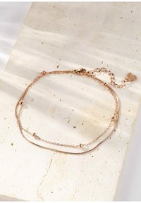 Bracciale in oro rosa con due catene, una liscia e l'altra a perline, dotato di chiusura a gancio e ciondolo a forma di cuore. Finitura texture.