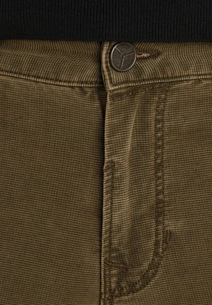 Tela marrón texturizada de pantalones que muestra un acanalado estrecho. Con un botón de metal y costuras en contraste a lo largo de la cinturilla y los bolsillos.