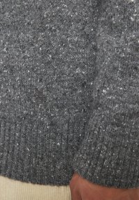 Grau gestrickter Pullover mit strukturiertem Muster, ausgestattet mit einem gerippten Saum und Bündchen. Kleines gesticktes Logo-Detail auf der Vorderseite.