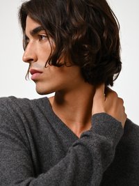 Harmaa V-pohjainen neule pehmeästä materiaalista, istuva malli, jossa on pitkät hihat ja ribbauslahkeet. Päällä henkilö, jolla on hajotut hiukset.