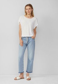 Witte, kortarmige shirt met opgerolde mouwen, gecombineerd met lichtblauwe, losse jeans met een trekkoord in de taille en witte schuifsandalen.