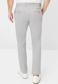 Pantaloni dritti grigi realizzati in tessuto misto cotone, con tasche posteriori con bottoni e una texture liscia. Indossati con sneaker bianche.