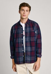 Camicia in flanella nei colori blu navy, rosso e grigio a quadri, con chiusura a bottoni, taschino sul petto e maniche arrotolate. Tessuto leggero.