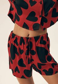 Red and black heart-patterned short pajama set, made of smooth fabric, featuring an elastic waistband and a loose-fitting top with short sleeves.