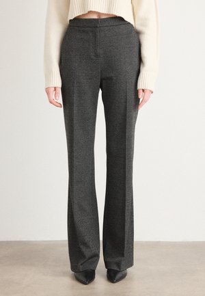 Grå skreddersydd bukser med et herringbone-mønster. Flat front med to sidelommer, utsvingt design og en jevn tekstur. Kombinert med svarte spisse sko.