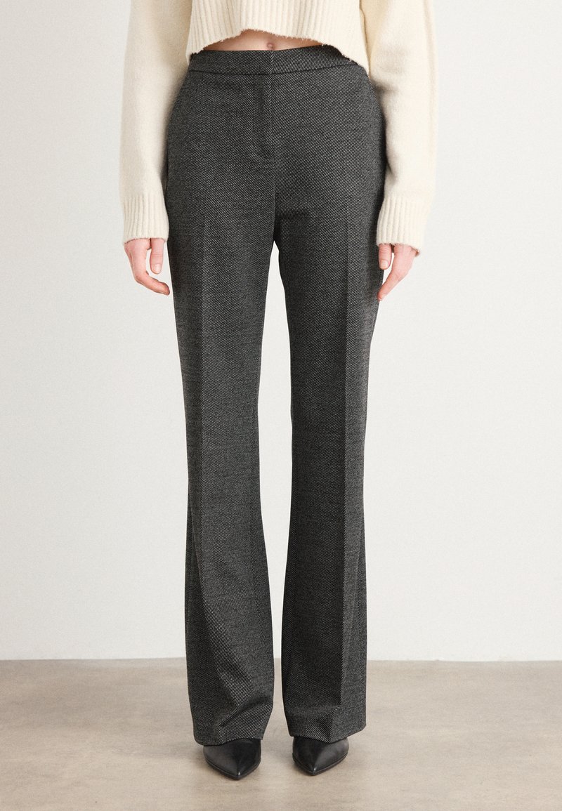 Grå skreddersydd bukser med et herringbone-mønster. Flat front med to sidelommer, utsvingt design og en jevn tekstur. Kombinert med svarte spisse sko.