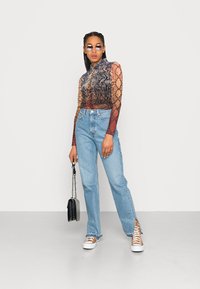 Camisola de mangas longas com um padrão de cobra multicolorido, combinada com uns jeans de perna reta de um azul claro. Uma bolsa preta e ténis completam o visual.