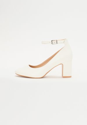 Hvid højhælet sko med spids tå, blokhæln og ankelrem. Glat overflade med en subtil glans og beige inderforing.