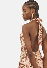 Vestido de tirantes en crema con patrones abstractos rojos. Presenta un escote abierto y detalle de lazo en el cuello. Fabricado en tejido ligero.