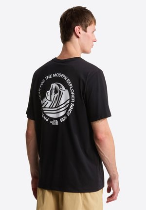 Camiseta negra de tela con un diseño gráfico de montañas y texto en la espalda. Mangas cortas y ajuste holgado. Material de algodón resistente.