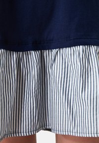 Marineblaue Baumwollbluse mit geradem Saum über einem plissierten Rock in horizontalen blau-weißen Streifen. Hat eine weiche Textur und ein lässiges Design.