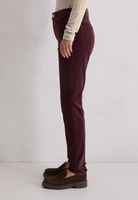Bordowe dopasowane jeansy z bocznymi kieszeniami i standardowym pasem, zestawione z ciemnobrązowymi butami wsuwanymi, widziane z boku.