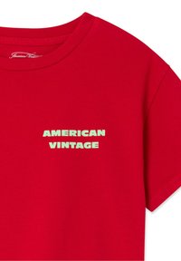 T-shirt rouge à manches courtes avec col rond et texte vert pâle "AMERICAN VINTAGE" imprimé sur la poitrine.