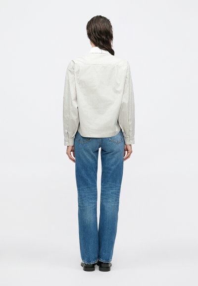 Light plaid button-up shirt with long sleeves, paired with blue straight-leg jeans and black shoes, viewed from the back.