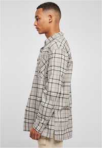 Grijze geblokte flanellen shirt met contrasterende zwart-witte lijnen, lange mouwen en een borstzak, met een ontspannen snit en zijsplitten.