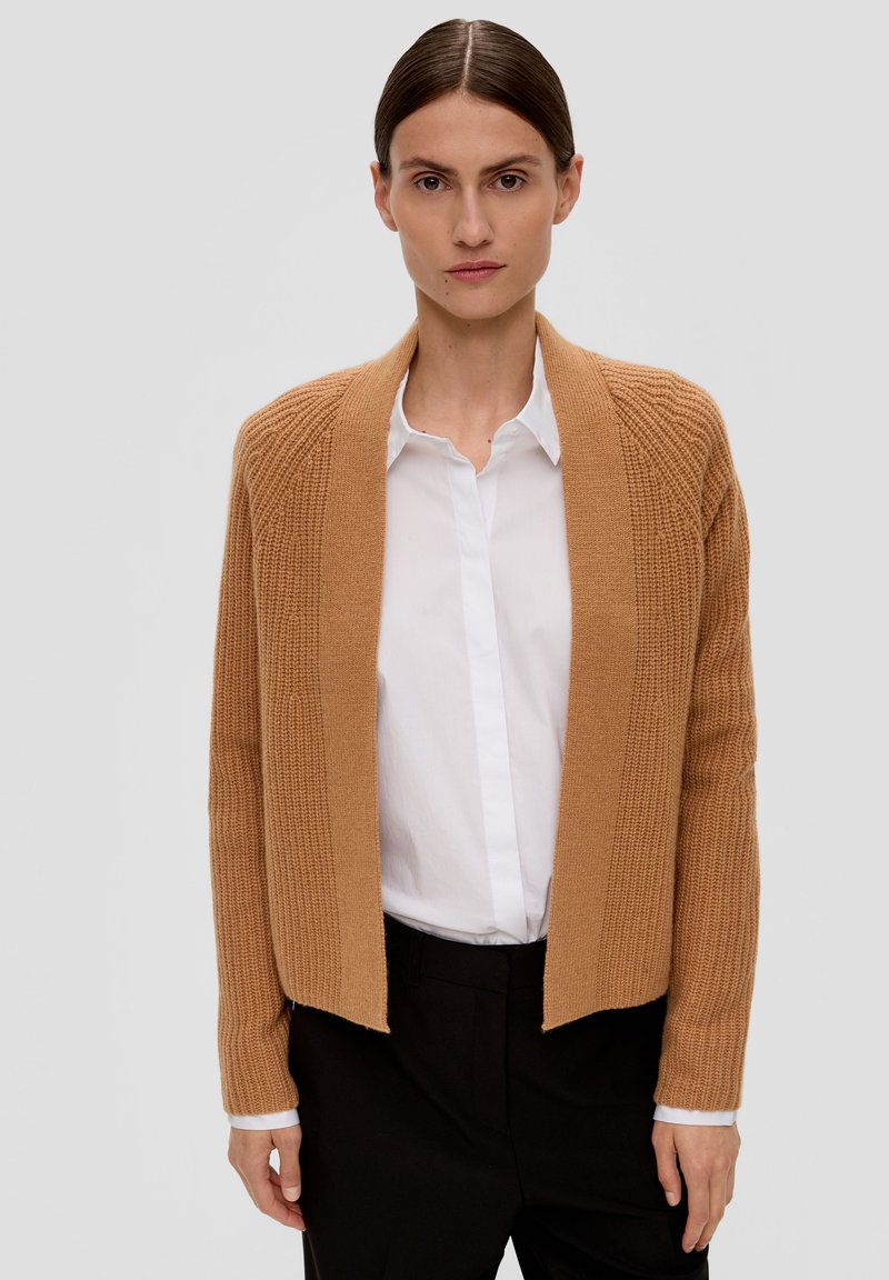 Beige Strickcardigan mit geripptem Textur, offenem Design und langen Ärmeln, kombiniert mit einem weißen Hemd mit Kragen und schwarzen Hosen.