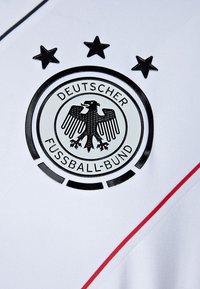 Biała koszulka sportowa z czarnym logo Deutscher Fußball-Bund oraz emblematem orła, z trzema gwiazdami powyżej i czerwonymi akcentami.