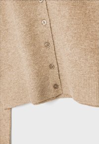 Beige pletený svetr s žebrovaným lemem, který má vpředu šest hnědých knoflíků a jemný, strukturovaný povrch.