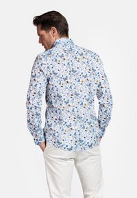 Chemise blanche à manches longues avec un motif floral comportant des fleurs bleues, des accents orange et des papillons. Fini avec un col classique.
