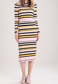 Abito a maniche lunghe con strisce orizzontali in rosa, nero e giallo. Vestibilità slim e lunghezza al ginocchio, abbinato a sneakers rosa chiaro.