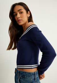 Mörkblå kortad tröja med bred vit och marinblå randig krage, stickad textur, långa ärmar och ribbad nederkant, kombinerad med denimshorts.