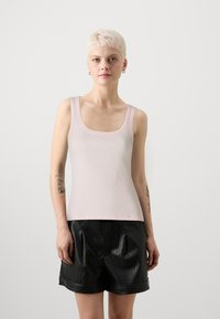 Lys rosa tank topp med firkantet utringning og ribbestruktur, kombinert med svarte skinnshorts med plisser og rullet kant.