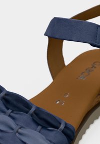Μπλε δερμάτινο σανδάλι με πλεγμένο σχέδιο λουριού, ανοιχτή μύτη και επενδυμένο καφέ πέλμα με ανάγλυφη επιγραφή μάρκας. Ρυθμιζόμενο λουρί αστραγάλου.