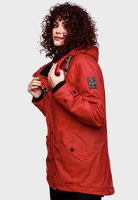 Röd vattentät parka med huva, dragsko och svarta detaljer. Har framfickor och en logotyp-patch på ärmen. Mjuk innervadding.