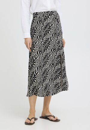 Naine, kes kannab musta-valget loomamustriga keskpikka seelikut, millel on külje peal lõhike, kombineeritud valge pika varrukaga särgi ja mustade sandaalidega.