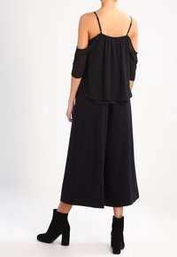 Top nero a spalle scoperte con spalline regolabili, abbinato a culotte nere a gamba larga e stivaletti neri in tessuto fino alla caviglia.