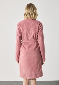 Rosa frotté badekåpe med lange ermer, belte i livet og en teksturert overflate, som faller til midt på låret. Bakvisning vist.