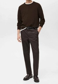 Brązowy sweter z okrągłym dekoltem, nałożony na biały shirt; w połączeniu z ciemnobrązowymi spodniami i brązowymi mokasynami. Prosty design, teksturowana tkanina.