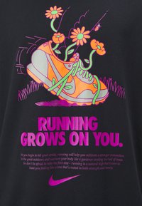 Černé tričko s ilustrací neónově oranžového teniska obklopeného květinami, s růžovým textem: "BĚHÁNÍ TI ROSTE NA TEBE." Logo Nike je součást�í designu.