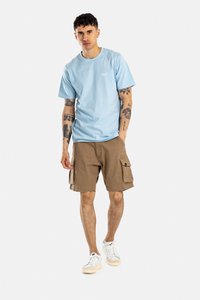 Camiseta de algodón color azul claro con cuello redondo, combinada con pantalones cortos de cargo marrones con múltiples bolsillos y zapatillas blancas con suela beige.