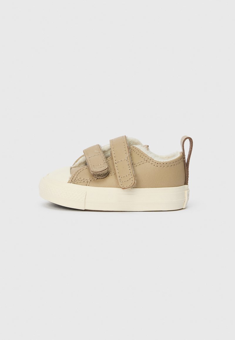 Pulka ādas toddler kedas ar diviem Velcro siksnām, krēmveida iekšējā oderē un baltu gumijas zoli. Apaļš purngals un aizmugures cilpa detaļa.