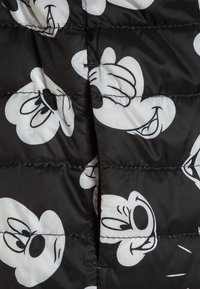 Czarna pikowana tkanina z dużymi białymi twarzami postaci z kreskówek o różnych wyrazach, przeszywana poziomymi rzędami z widocznymi szwami.