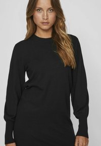 Zwart gebreide trui-jurk met lange pofmouwen, een geribbelde halslijn en manchetten, en een gladde textuur. Ontworpen voor een aansluitende silhouet.