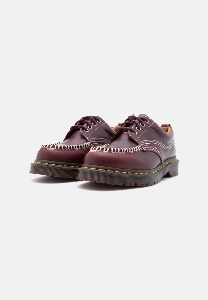 Pair of dark burgundy leather lace-up shoes with white stitching and thick black soles with yellow welt stitching.