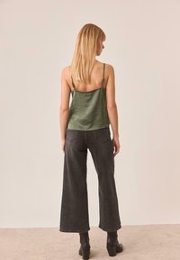 Camisola de satén verde oliva con tirantes finos ajustables, combinada con jeans de pierna ancha de cintura alta negros y botas de tacón negro hasta el tobillo.