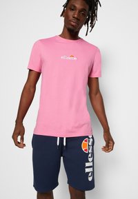 Rosa Kurzarm-T-Shirt mit dezentem Logo; kombiniert mit marineblauen Shorts, die ein kontrastierendes Logo und einen Kordelzugbund aufweisen. Weicher Stoff, lässige Passform.